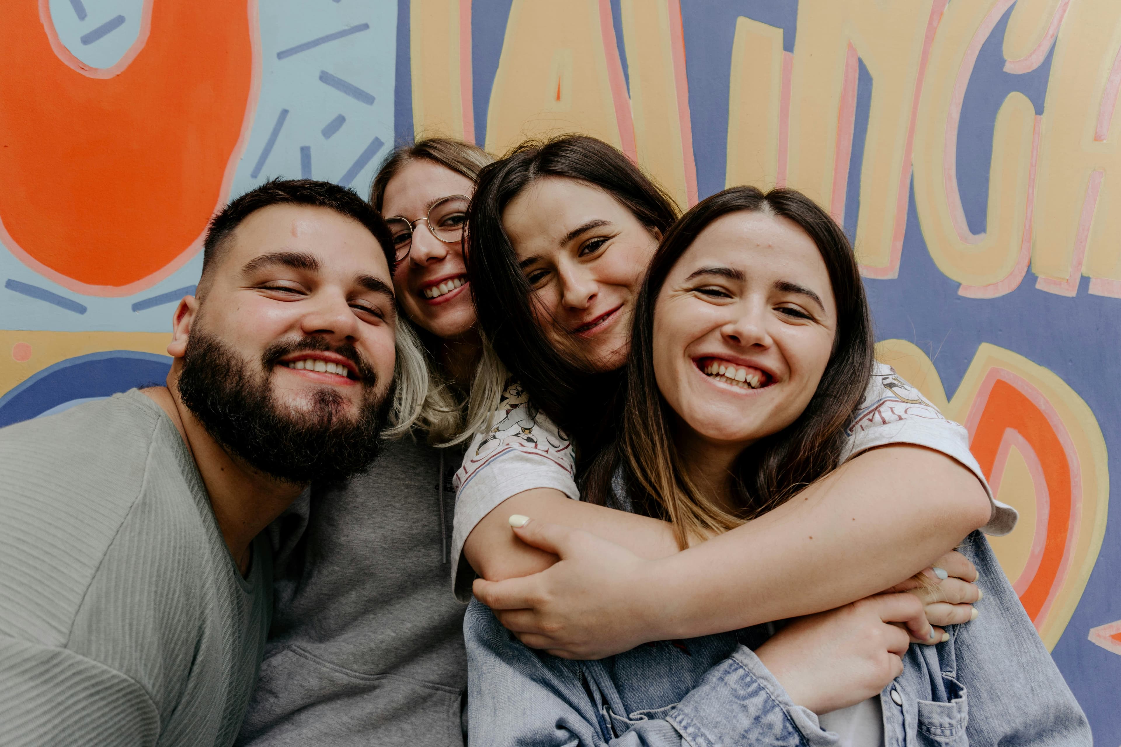 Grupo de amigos abrazados sonriendo frente a un mural colorido